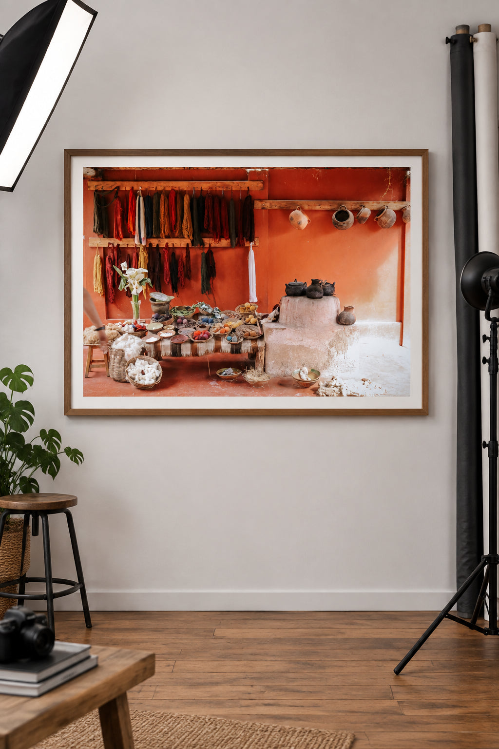 A rustic interior scene in South America with a table covered in colorful, naturally dyed yarns, wool bundles, and small bowls, set against a terracotta wall with hanging colorful textiles and clay pots.