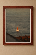 Sailboat with an amber sail on rippling water, displayed in a reddish-brown wooden frame with a white border