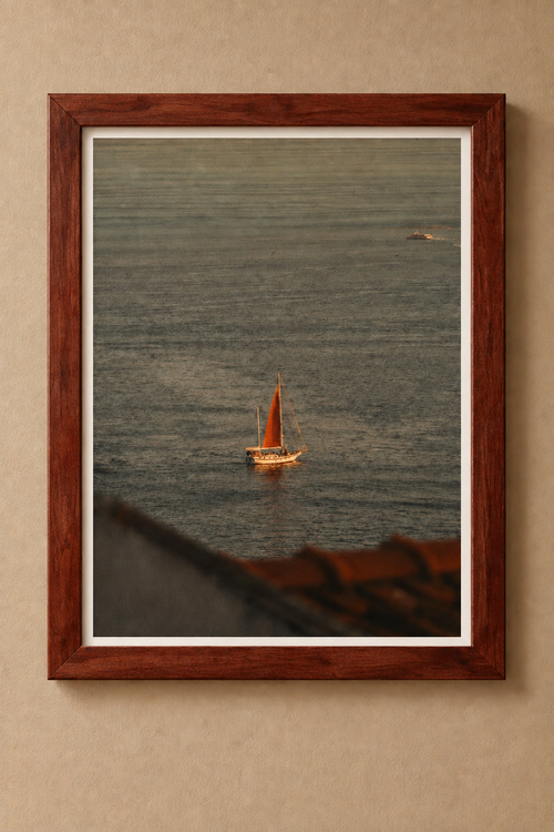 Sailboat with an amber sail on rippling water, displayed in a reddish-brown wooden frame with a white border